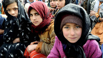 Village girls wait as the Afghan National Police unload a shipment of humanitarian aid in Herat province in 2009. Food, winter clothing and supplies were delivered to 300 villagers. ISAF photo by U.S. Air Force TSgt Laura K. Smith.